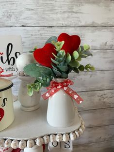 a white table topped with two vases filled with flowers and hearts next to a sign