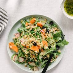 a white plate topped with salad next to a bowl of pesto and carrots