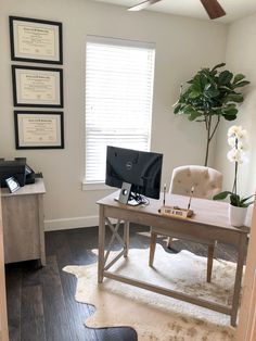 a desk with a computer on it in front of a window and a potted plant