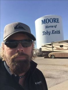 a man wearing sunglasses and a hat standing in front of a sign for moore home of tobby ketth