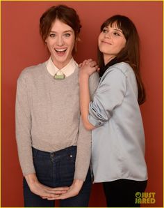 two women standing next to each other in front of a red wall with their arms around one another