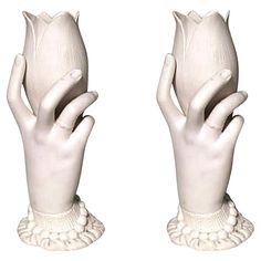 two white ceramic hands holding flowers on top of each other