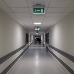 an empty hospital hallway with signs on the walls and people walking down the corridor between them