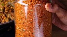 a person is holding a jar full of red chili seasoning next to a black pot