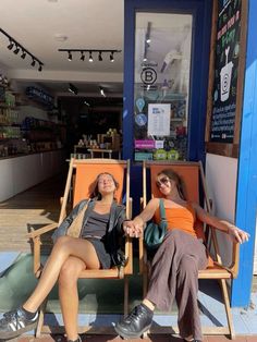 two women sitting in chairs outside of a store front with their feet up on the ground