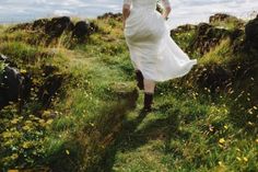 a woman in a white dress is walking up a hill with her back to the camera