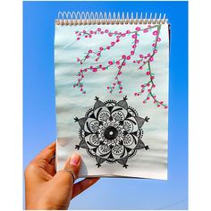 a hand holding up a spiral notebook with an intricate design on the cover and string attached to it