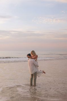 a man holding a woman in his arms while standing on the beach near the ocean