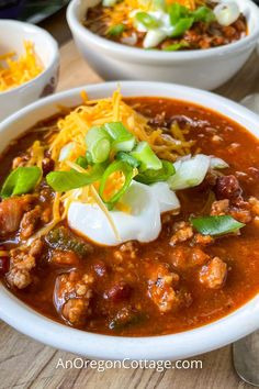 two bowls of chili and cheese soup on a wooden table