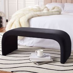 a black bench sitting on top of a rug next to a white bed with pillows