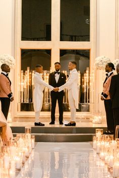 two men in tuxedos shaking hands at the end of a ceremony with candles