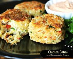 three crab cakes on a black plate with dipping sauce in the bowl next to it