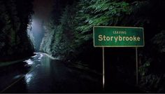 a sign that is in the middle of a road near some trees and water at night