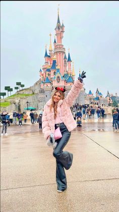 a woman posing in front of a castle with her arms up and hands out to the side