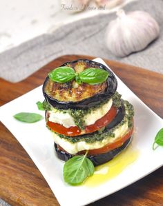 a stack of food sitting on top of a white plate next to garlic and green leaves