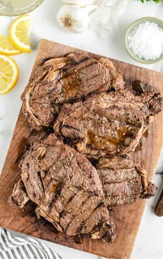 sliced steak on a cutting board with garlic and lemons