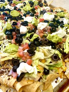 a pizza topped with lettuce, black olives and tomatoes next to tortilla chips