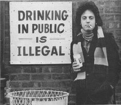 a man standing next to a sign that says drinking in public is illegal