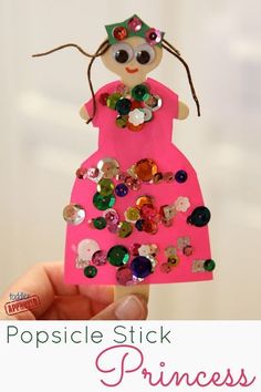 a hand holding up a pink paper doll with lots of sequins on it