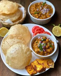 some food is on a white plate and sits next to other dishes with breads