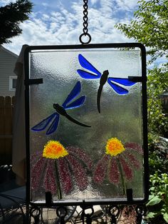 a stained glass window with two blue dragonflies on it's face and flowers in the foreground