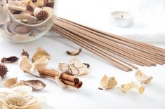 an assortment of dried flowers and sticks on a white surface with a candle in the background