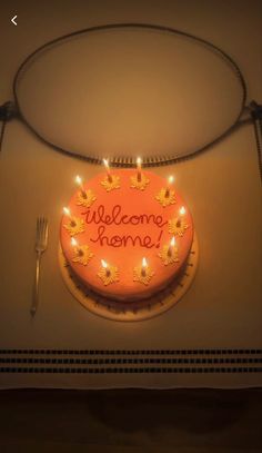 a cake with lit candles on it sitting next to a fork and knife in front of a sign that says welcome home