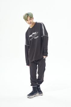 a young man with green hair standing in front of a white background wearing a black sweatshirt and sweatpants