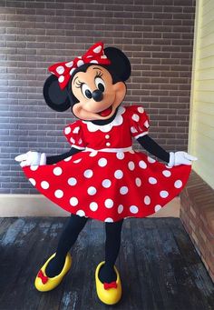 a minnie mouse costume is standing in front of a brick wall wearing a red and white polka dot dress