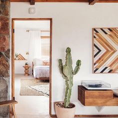 a cactus in a pot sitting next to a stone wall near a bed and desk