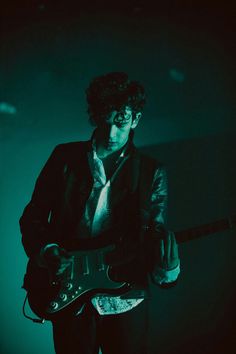 a man playing an electric guitar while wearing a black suit and tie with his hands on his hips