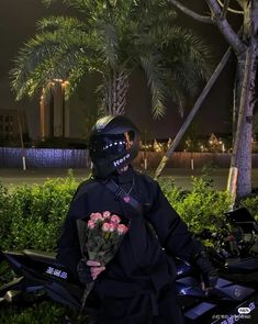 a man in black jacket sitting on motorcycle holding flowers and wearing helmet with palm trees behind him