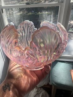 a hand holding a pink glass bowl in front of a window with the sun shining through it