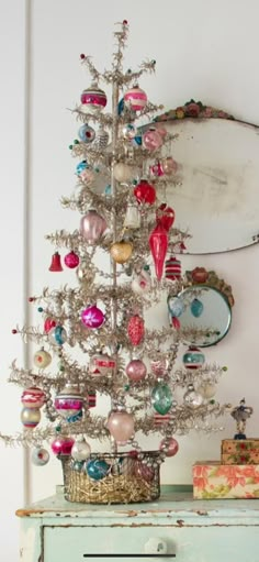 a small white christmas tree sitting on top of a blue dresser next to a mirror