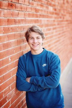 a man leaning against a brick wall with his arms crossed and smiling at the camera