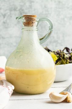 a glass bottle filled with dressing next to a bowl of salad and utensils