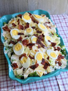 a salad with hard boiled eggs and bacon in it on a blue platter sitting on a checkered table cloth