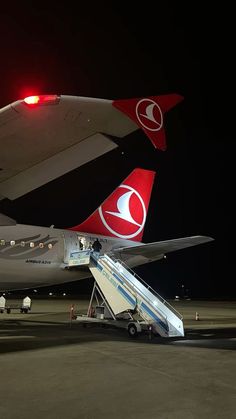 two airplanes are parked on the tarmac at night with their doors open and stairs down