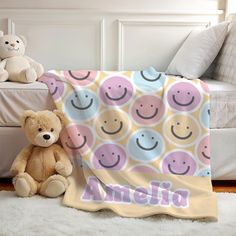 a teddy bear sitting next to a blanket with smiley faces on it