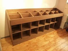 a wooden shelf filled with lots of compartments on top of a hard wood floor next to a white wall