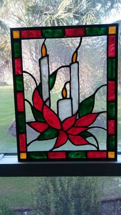 a stained glass window with two candles and a flower in the center, sitting on a windowsill