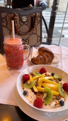 a white plate topped with fruit and granola next to a cup of coffee on a table