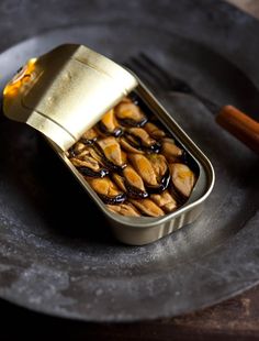 a metal tray with some food in it on top of a plate next to a knife and fork