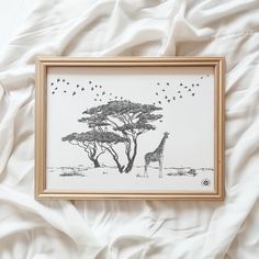 a giraffe standing next to a tree on top of a white bed sheet