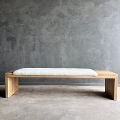 a wooden bench sitting in front of a gray wall with concrete floor and walls behind it