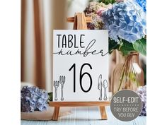 a table number sign sitting on top of a wooden easel next to blue flowers