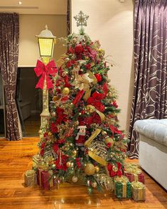 a decorated christmas tree in a living room with red and gold ornaments on the top