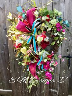 a wreath with flowers and ribbons hanging on a fence