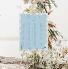 a blue and white wedding seating sign on a wooden easel with flowers in the background