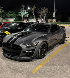 two cars parked in a parking lot next to each other at night with people looking on